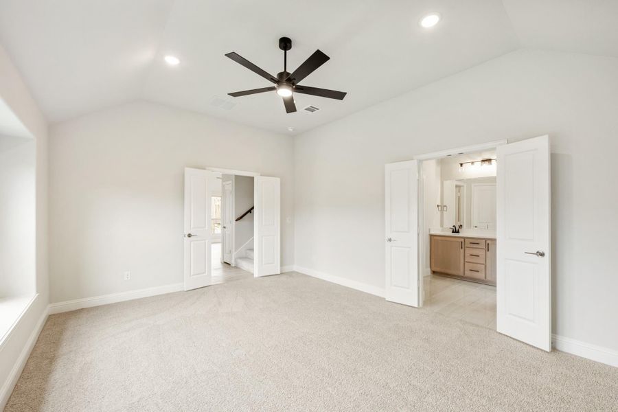 Empty master bedroom with carpet, ceiling fan, and open doors to ensuite bathroom and hallway