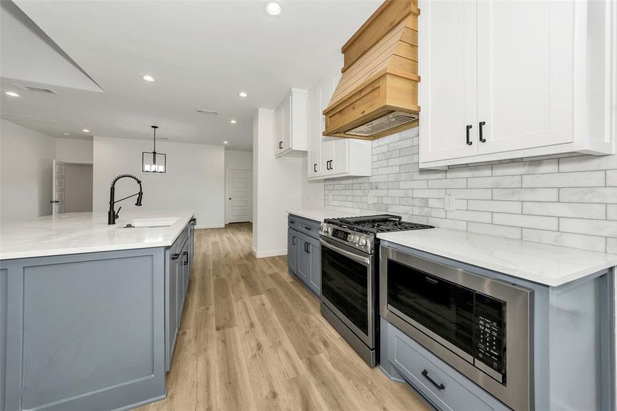 Kitchen with a sink, appliances with stainless steel finishes, custom exhaust hood, tasteful backsplash, and white cabinetry Kitchen with a sink, appliances with stainless steel finishes, custom exhaust hood, tasteful backsplash, and white cabinetry