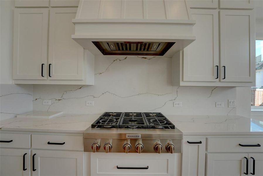 Kitchen featuring stainless steel gas cooktop, premium range hood, backsplash, and white cabinetry