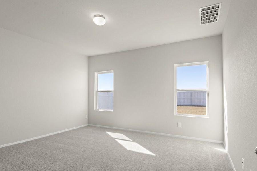 Image of a primary bedroom with cream walls, tan carpeting, two windows, and white trim Image of a primary bedroom with cream walls, tan carpeting, two windows, and white trim