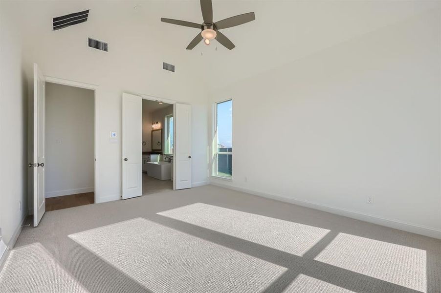 Bedroom with connected bathroom, ceiling fan, high vaulted ceiling, and light carpet