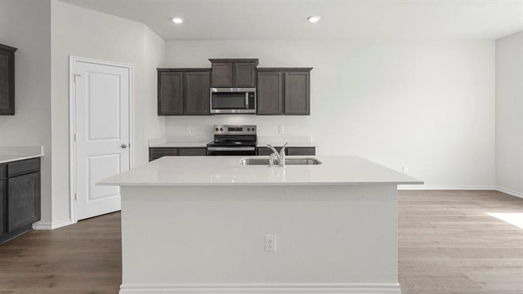 The kitchen features dark wood cabinetry, stainless steel appliances, and a central island with a sink and white countertop