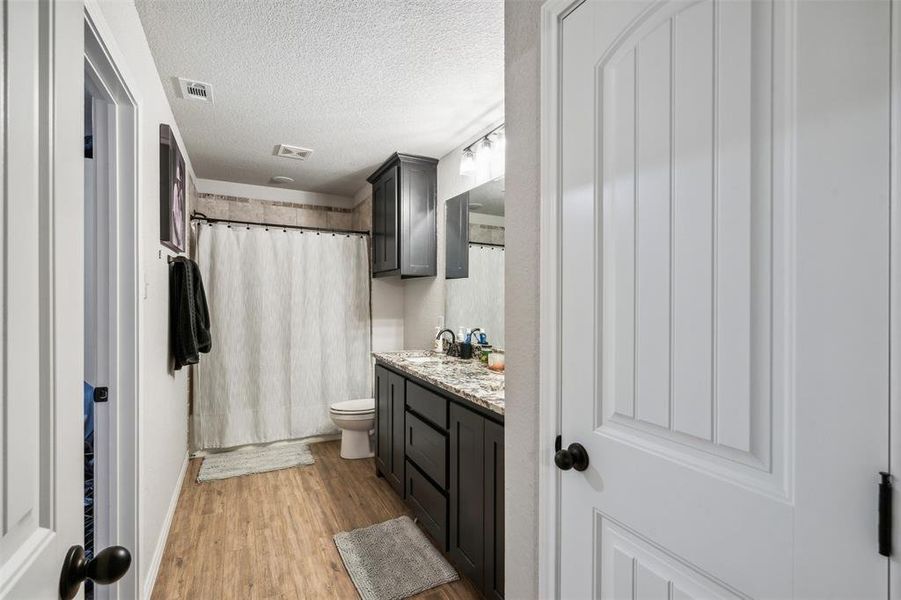 Bathroom with vanity, a shower with curtain, hardwood / wood-style flooring, toilet, and a textured ceiling