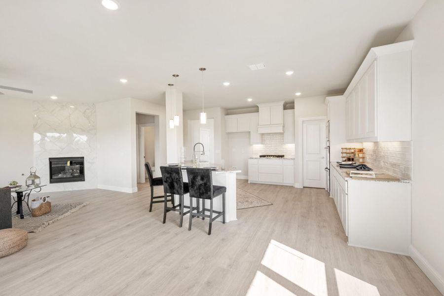 Open-concept kitchen with white cabinets, center island, and light wood floors, open to living area with fireplace.