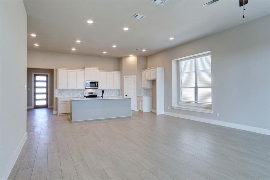 Kitchen featuring appliances with stainless steel finishes, tasteful backsplash, white cabinetry, a kitchen island with sink, and ceiling fan