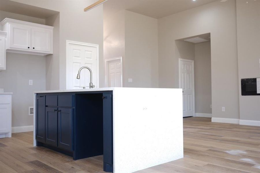 Kitchen with white cabinetry, light wood finished floors, blue cabinets, and a center island with sink Kitchen with white cabinetry, light wood finished floors, blue cabinets, and a center island with sink