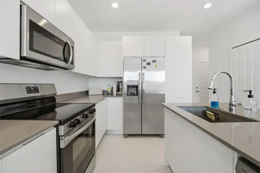 Kitchen featuring flat-panel white cabinetry, stainless steel appliances, quartz countertops, an undermount sink with a gooseneck faucet, and tile flooring