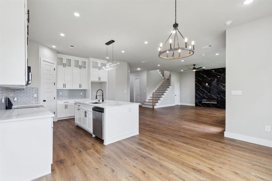 Kitchen with light wood-type flooring, pendant lighting, ceiling fan with notable chandelier, an island with sink, and appliances with stainless steel finishes