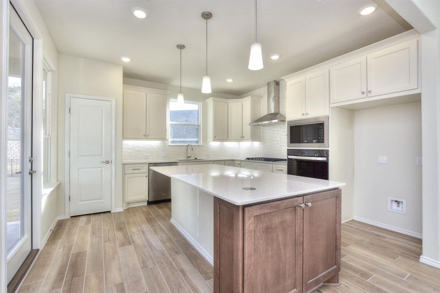 Kitchen featuring wood finish floors, a sink, appliances with stainless steel finishes, wall chimney exhaust hood, and backsplash