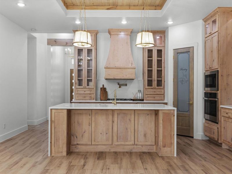Kitchen with a tray ceiling, glass insert cabinets, hanging light fixtures, and recessed lighting