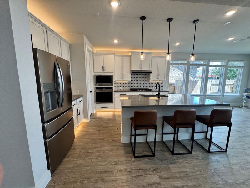 Kitchen with appliances with stainless steel finishes, pendant lighting, white cabinets, a kitchen breakfast bar, and recessed lighting