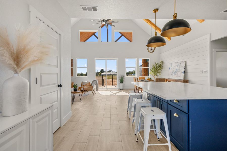 Kitchen featuring blue cabinets, high vaulted ceiling, ceiling fan, decorative light fixtures, and a breakfast bar area