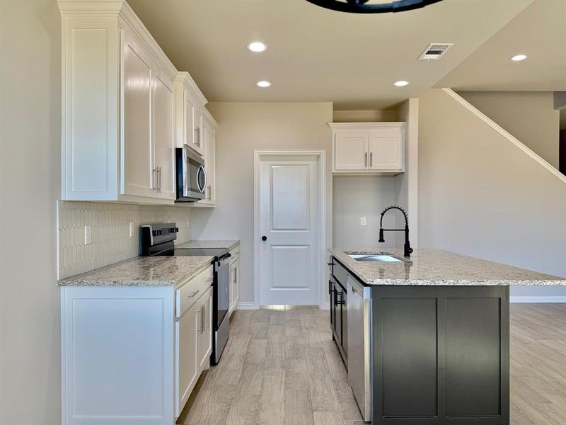 Kitchen featuring white cabinetry, stainless steel appliances, a kitchen island with sink, and sink