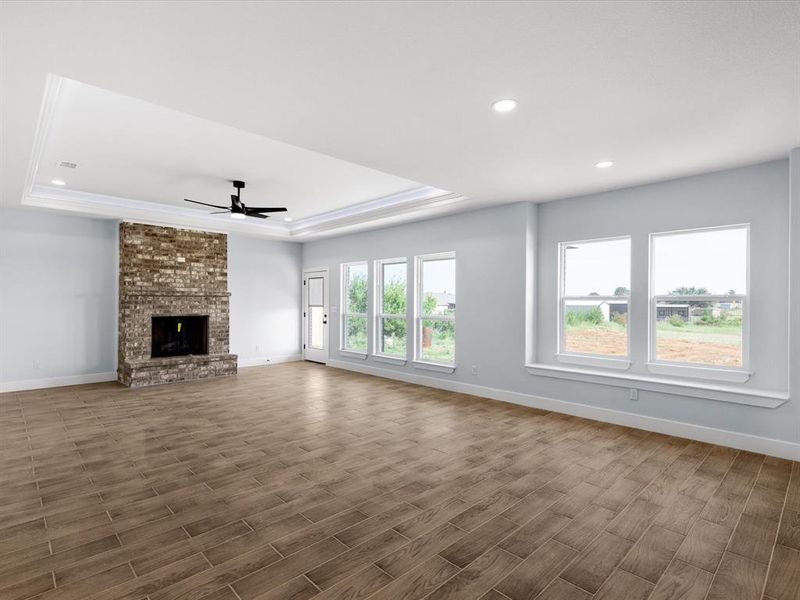 Unfurnished living room with dark wood-style floors, a tray ceiling, ceiling fan, a brick fireplace, and recessed lighting