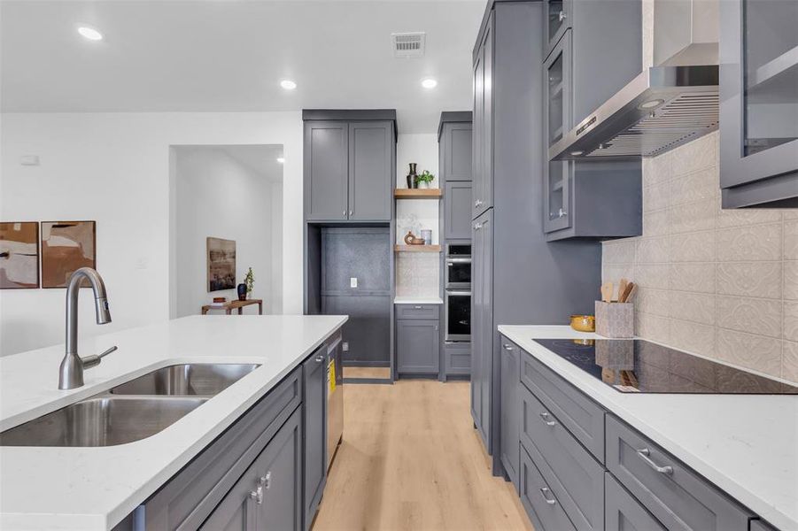 Kitchen featuring tasteful backsplash, light wood-type flooring, light stone counters, wall chimney range hood, and black electric cooktop Kitchen featuring tasteful backsplash, light wood-type flooring, light stone counters, wall chimney range hood, and black electric cooktop