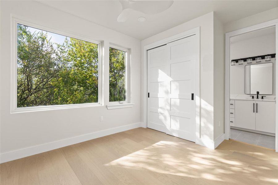 Hardwood floors and large windows framing lush tree views define this peaceful bedroom.