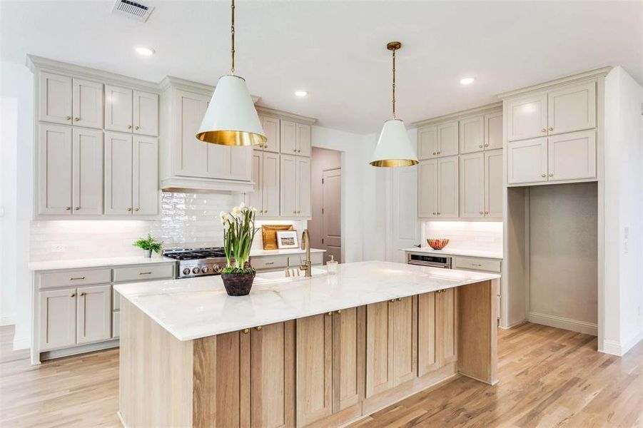 Kitchen featuring decorative backsplash, light stone countertops, light wood-style flooring, a kitchen island with sink, and recessed lighting