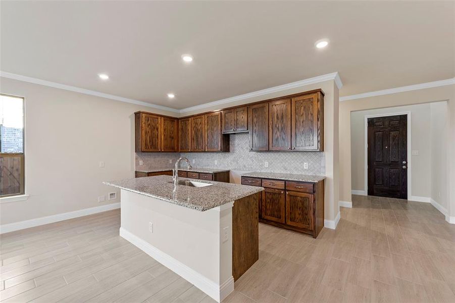 Kitchen featuring backsplash, sink, ornamental molding, an island with sink, and light stone counters