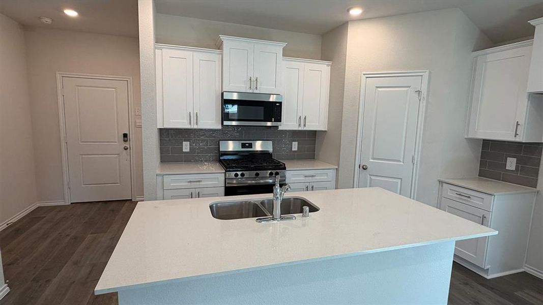 Modern kitchen featuring a large island with an undermount dual-basin sink, white shaker cabinetry, stainless steel appliances, a subway tile backsplash, and wood-finish flooring