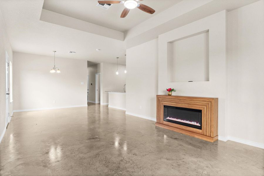 Unfurnished living room with a glass covered fireplace, finished concrete floors, ceiling fan, a raised ceiling, and a chandelier