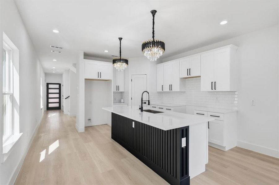 Open-concept kitchen featuring a black slatted island with white countertop, white shaker cabinetry, subway tile backsplash, and two tiered crystal chandeliers Open-concept kitchen featuring a black slatted island with white countertop, white shaker cabinetry, subway tile backsplash, and two tiered crystal chandeliers