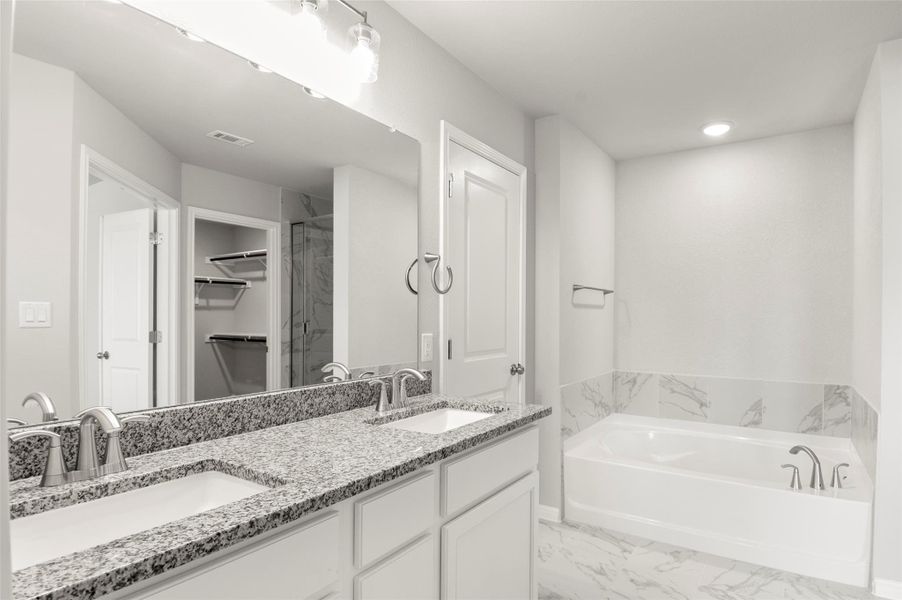 Bathroom featuring a garden tub, marble look tiles, double vanity, and a walk in closet