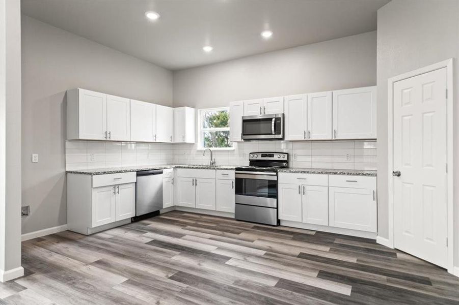 Kitchen featuring white cabinets, appliances with stainless steel finishes, light stone counters, and a high ceiling