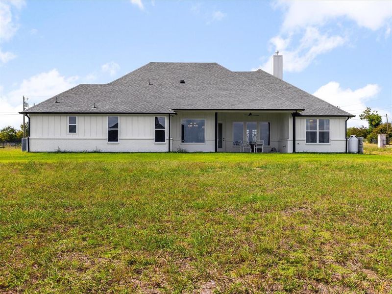 Back of house featuring a yard, board and batten siding, a chimney, a patio area, and roof with shingles Back of house featuring a yard, board and batten siding, a chimney, a patio area, and roof with shingles