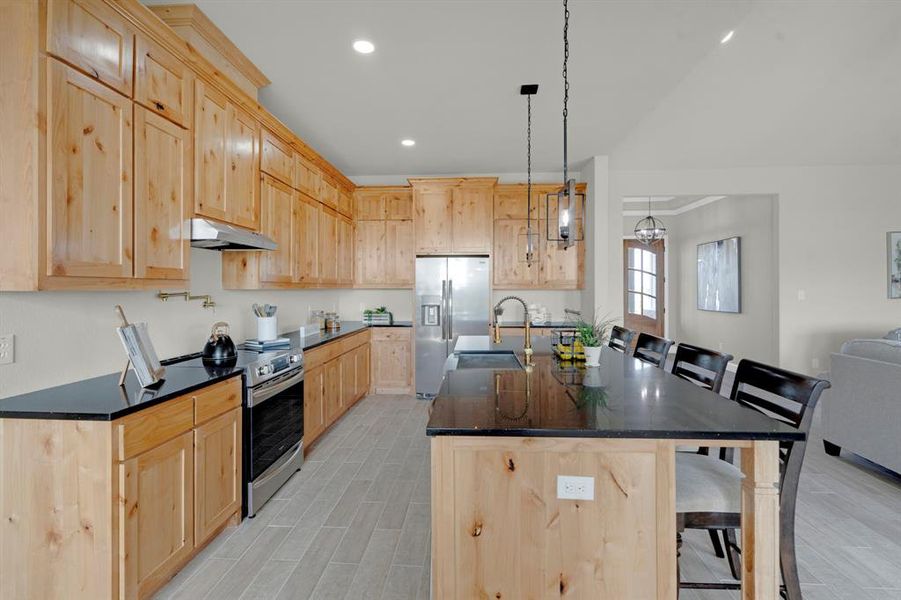 Kitchen featuring light brown cabinetry, appliances with stainless steel finishes, sink, a breakfast bar area, and pendant lighting