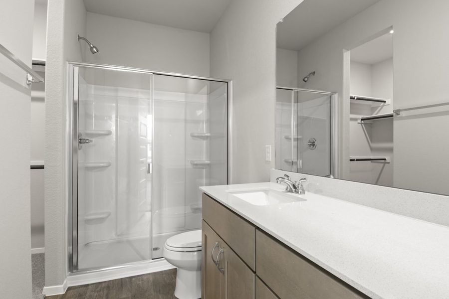 Image of primary bathroom with a walk in shower and brown cabinets and a mirror with a white counter vanity