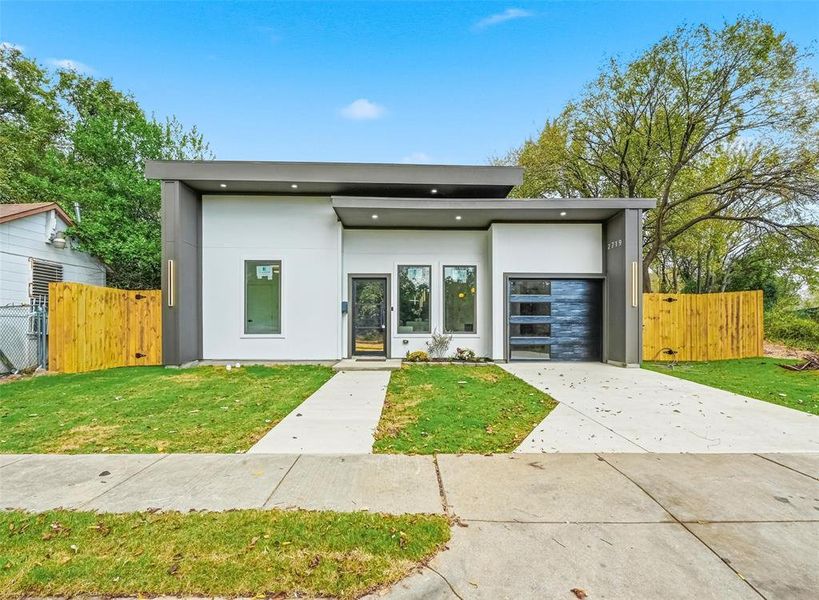 Modern home featuring privacy gate, security lighting, concrete driveway, and an attached garage Modern home featuring privacy gate, security lighting, concrete driveway, and an attached garage