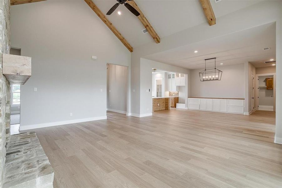 Unfurnished living room with high vaulted ceiling, beam ceiling, light wood-type flooring, and ceiling fan with notable chandelier