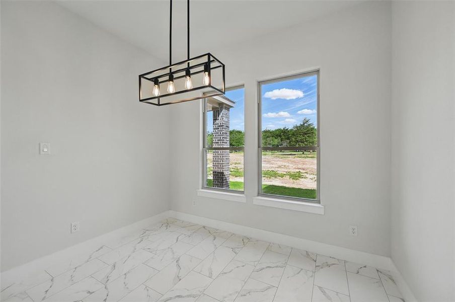 Unfurnished dining area featuring baseboards, a chandelier, and marble look tile flooring Unfurnished dining area featuring baseboards, a chandelier, and marble look tile flooring