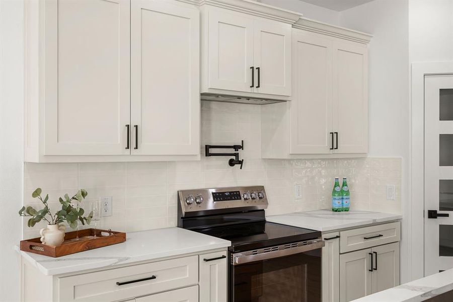 Kitchen with white cabinets, electric range, light stone counters, and tasteful backsplash