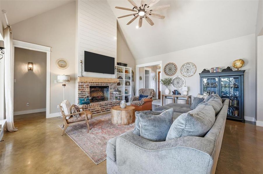 Living area featuring high vaulted ceiling, concrete flooring, ceiling fan, and a fireplace Living area featuring high vaulted ceiling, concrete flooring, ceiling fan, and a fireplace