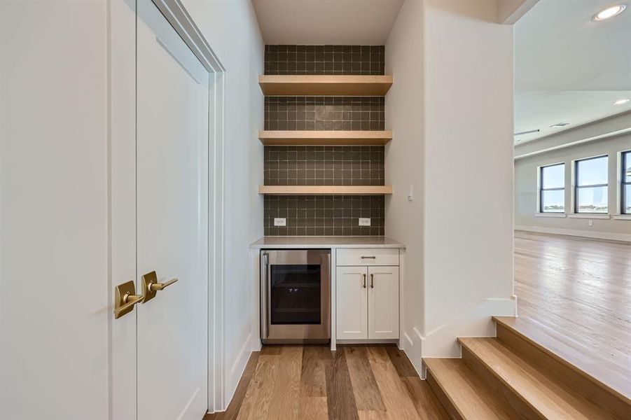 Bar with beverage cooler, white cabinetry, tasteful backsplash, and light hardwood / wood-style flooring