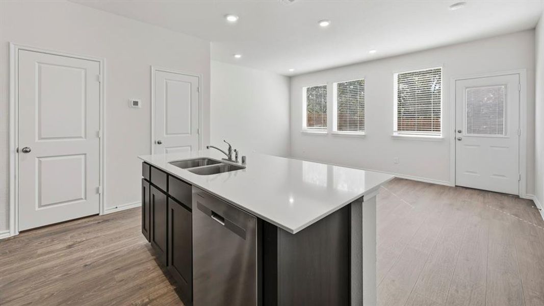 Kitchen featuring stainless steel dishwasher, an island with sink, light wood finished floors, light stone countertops, and recessed lighting
