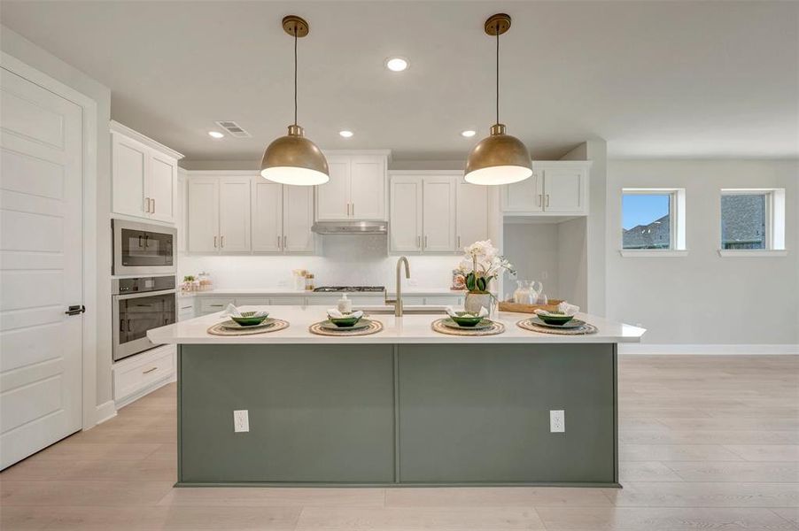 Expansive kitchen island with a light-toned countertop, complemented by two brass-toned pendant lights