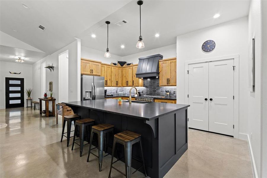 Kitchen featuring stainless steel appliances, a center island with sink, tasteful backsplash, decorative light fixtures, and finished concrete floors