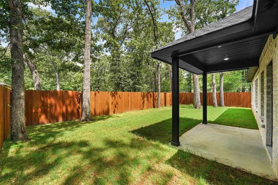 Expansive backyard featuring a covered patio, concrete slab, brick exterior, full wood privacy fence, and mature trees Expansive backyard featuring a covered patio, concrete slab, brick exterior, full wood privacy fence, and mature trees