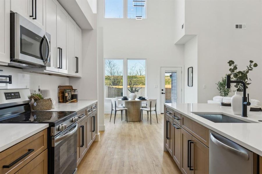 Kitchen featuring sink, white cabinetry, stainless steel appliances, and a towering ceiling