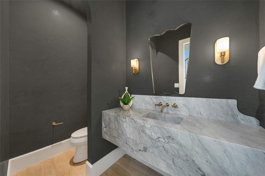 Powder room featuring a floating marble vanity with integrated sink, brass wall-mounted faucet, and two brass sconces