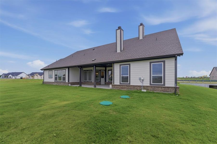 Rear exterior featuring an expansive green lawn, covered patio, multiple windows, and two prominent chimneys