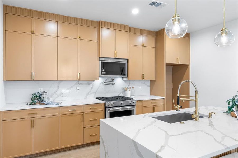 Kitchen featuring light stone counters, stainless steel appliances, decorative light fixtures, and backsplash