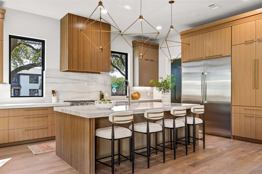 Kitchen with built in refrigerator, light stone countertops, a kitchen breakfast bar, hanging light fixtures, and light wood finished floors Kitchen with built in refrigerator, light stone countertops, a kitchen breakfast bar, hanging light fixtures, and light wood finished floors