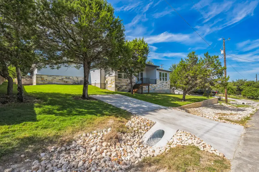 View of property hidden behind natural elements featuring stone siding, a front yard, stucco siding, and stairway