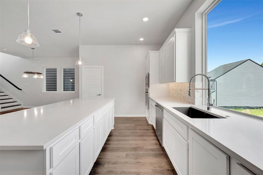 Modern kitchen featuring an expansive island with white cabinetry, wood-finish flooring, a large window, a stainless steel dishwasher, and a built-in oven