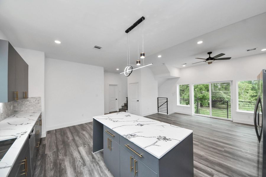 This modern open-concept kitchen and living space features sleek cabinetry, marble countertops, and stylish light fixtures. Large windows offer plenty of natural light and views of greenery, while the wood-look flooring adds warmth. The space is bright, airy, and perfect for entertaining. This modern open-concept kitchen and living space features sleek cabinetry, marble countertops, and stylish light fixtures. Large windows offer plenty of natural light and views of greenery, while the wood-look flooring adds warmth. The space is bright, airy, and perfect for entertaining.