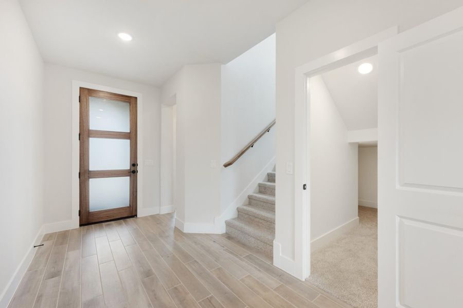 Entryway with wood-panel glass door, light hardwood floors, and carpeted staircase leading upstairs