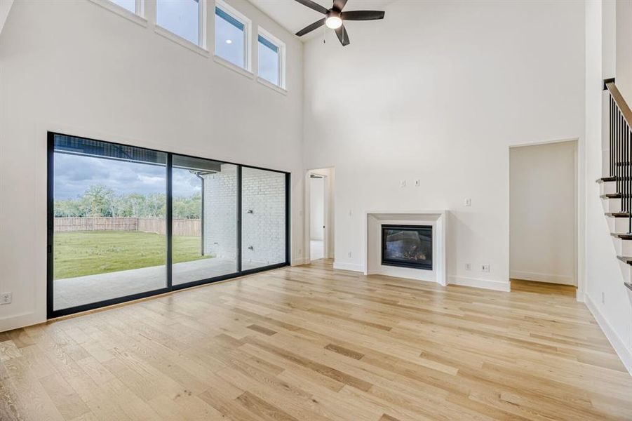 Unfurnished living room featuring plenty of natural light, light wood-type flooring, ceiling fan, a glass covered fireplace, and a high ceiling